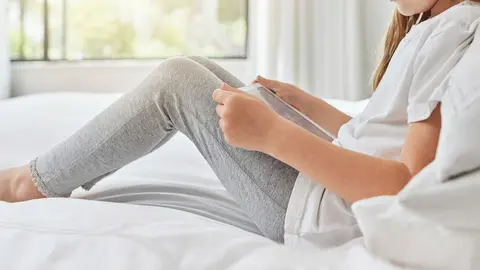 Little girl, reading and relax with tablet on bed for ebook, entertainment or online browsing at home. Young child, female person or kid with technology in bedroom for research, app or social media